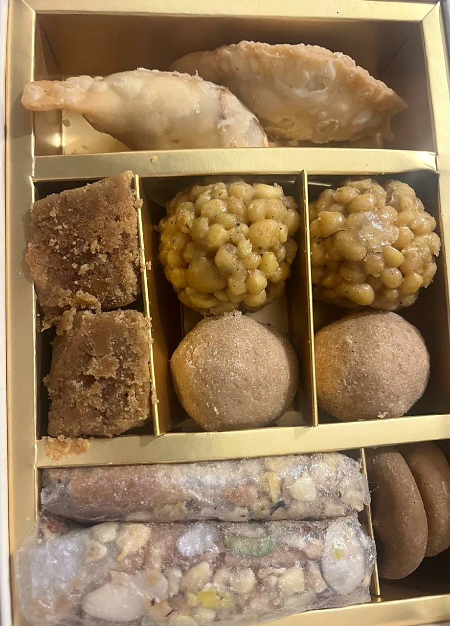 An open Misthi box: dryfruit gajjikaya, mysore pak, boondi laddus, sunnundalu, pootharekulu and palakova in a gold tray
